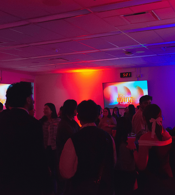 People socializing at a colorful indoor event with neon lighting and presentation screens